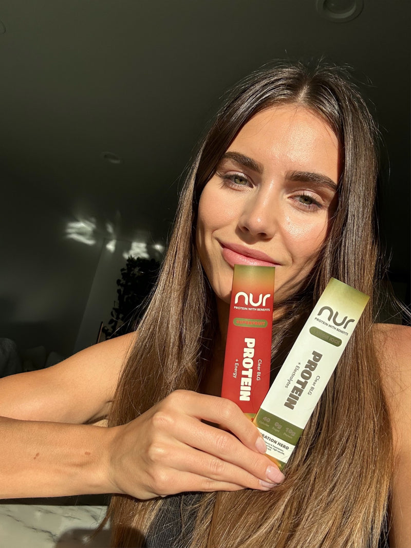 Woman holding two Nur protein bars in different flavors under natural sunlight.